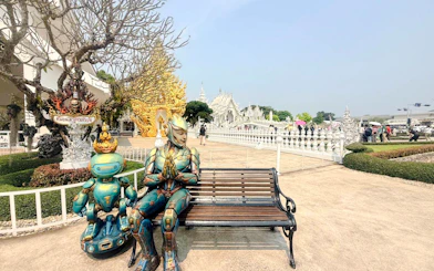 Robotic statues near White Temple, Chiang Rai, with intricate architecture in the background.