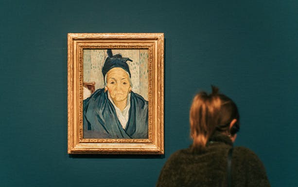 Painting of an elderly woman in a museum with a visitor observing.