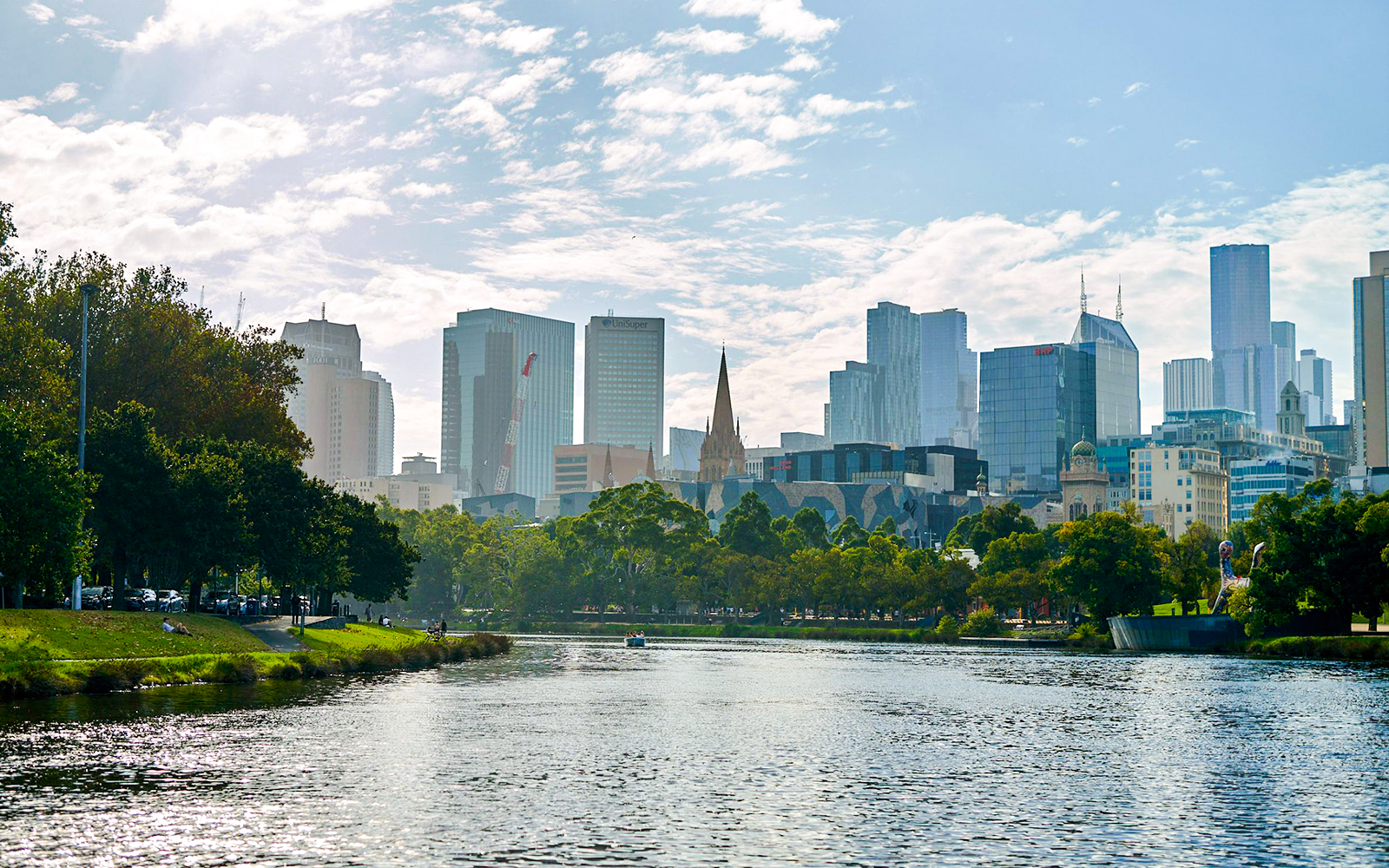 Melbourne skyline viewed from Yarra River, featuring cityscape and riverbank greenery.