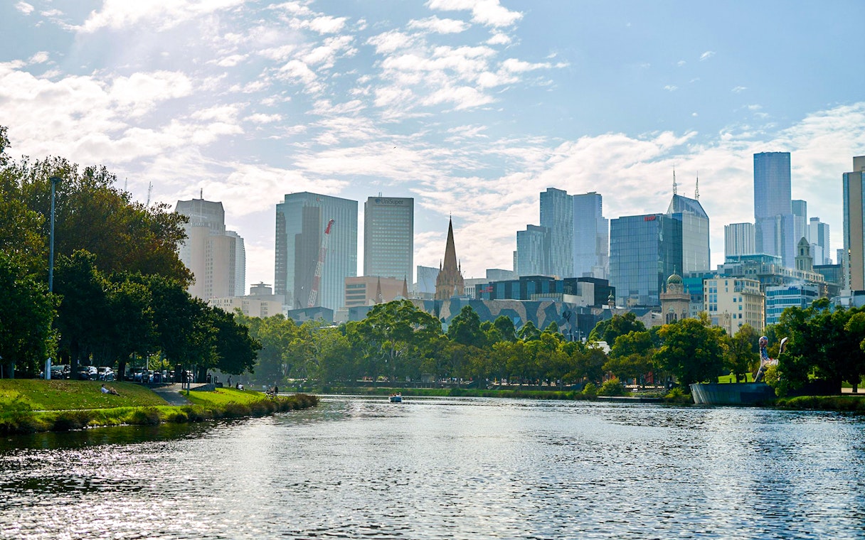 Melbourne skyline viewed from Yarra River, featuring cityscape and riverbank greenery.