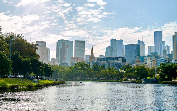 Melbourne skyline viewed from Yarra River, featuring cityscape and riverbank greenery.