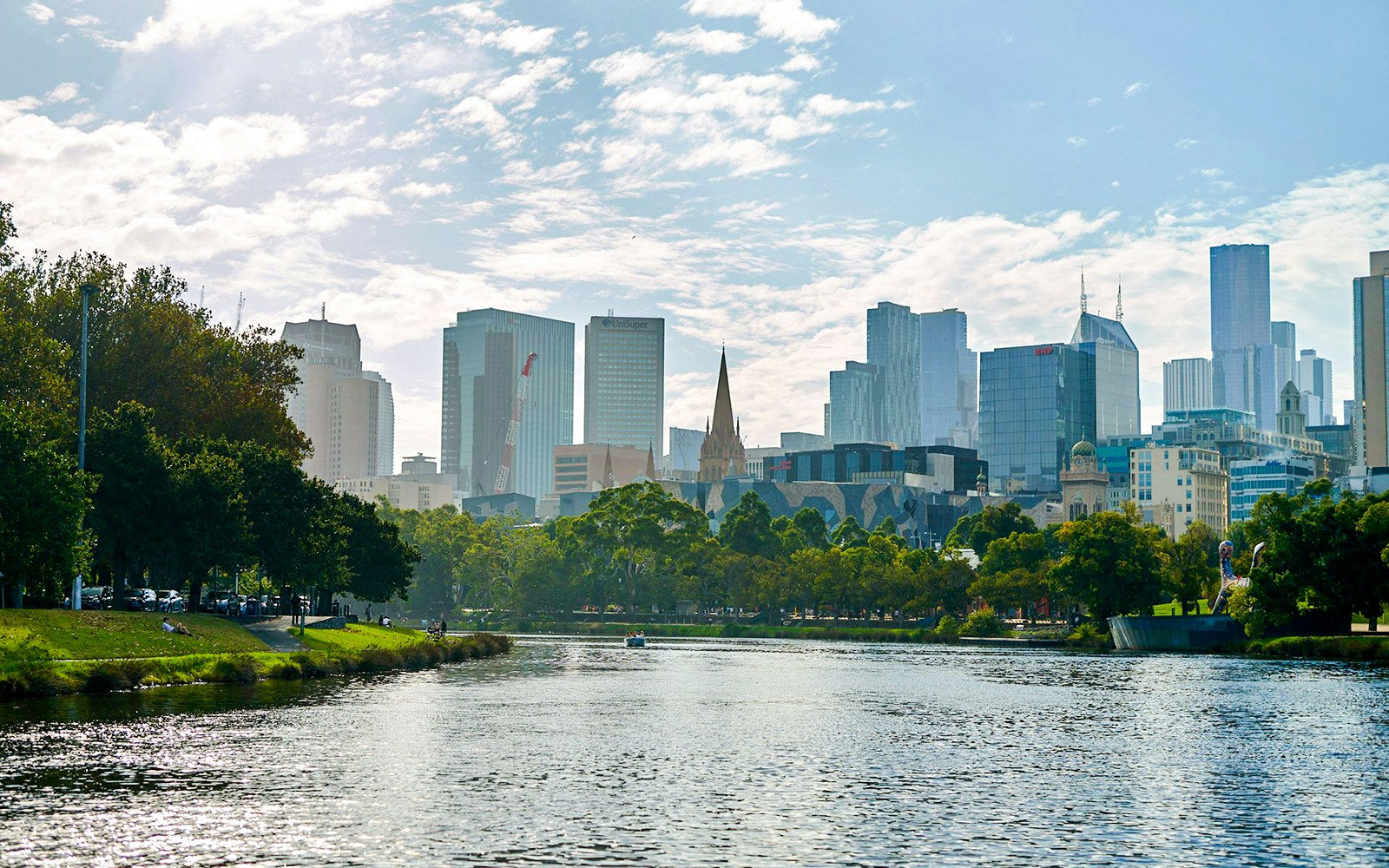 Melbourne skyline viewed from Yarra River, featuring cityscape and riverbank greenery.