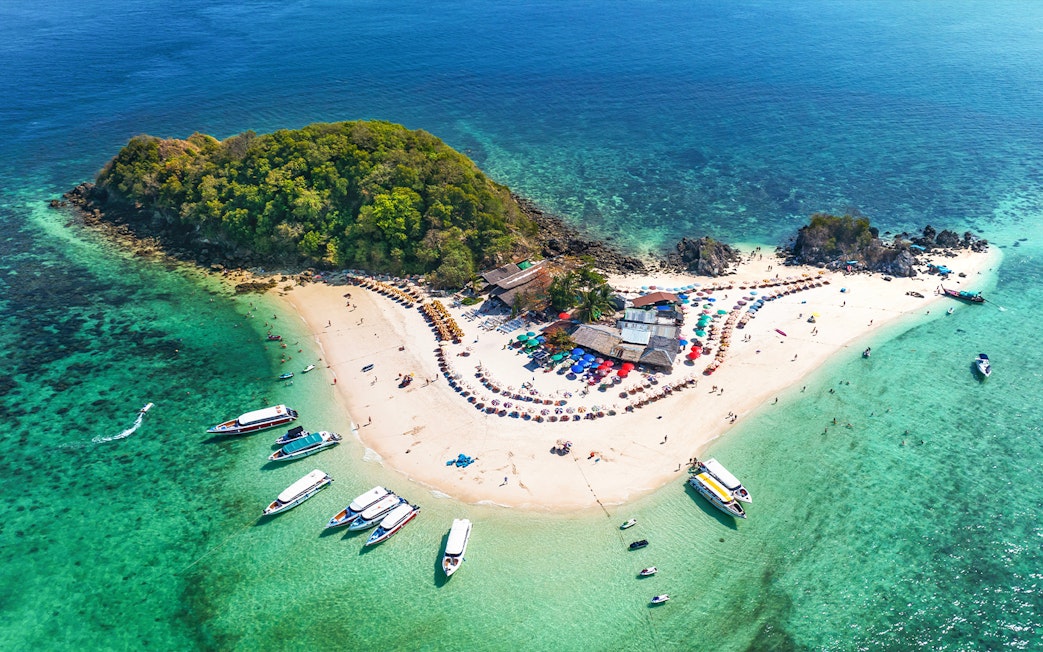 Aerial view of Khai Island, Thailand, with boats, beach umbrellas, and lush greenery.