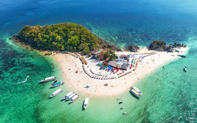 Aerial view of Khai Island, Thailand, with boats, beach umbrellas, and lush greenery.