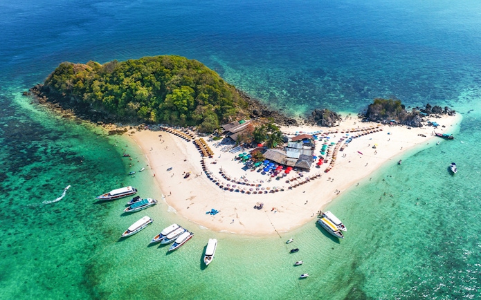 Aerial view of Khai Island, Thailand, with boats, beach umbrellas, and lush greenery.