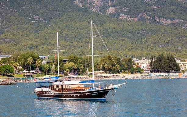 Boat sailing near Phaselis with lush mountains in the background, Antalya tour.