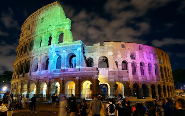 Colosseum illuminated with colorful lights at night, Rome, Italy.