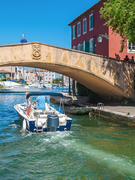 Boat passing under a stone bridge in Port Grimaud during St Tropez sightseeing tour.