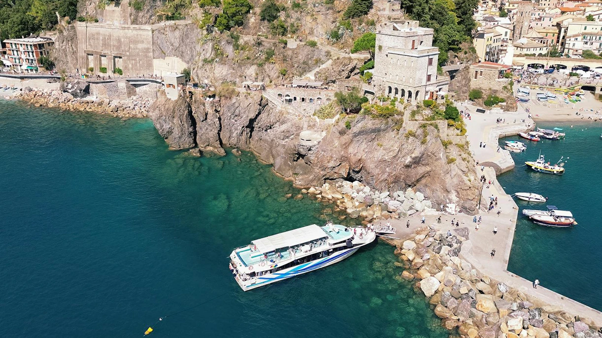 Cinque Terre cruise boat docked near rocky coastline with village in background.