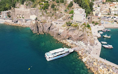 Cinque Terre cruise boat docked near rocky coastline with village in background.