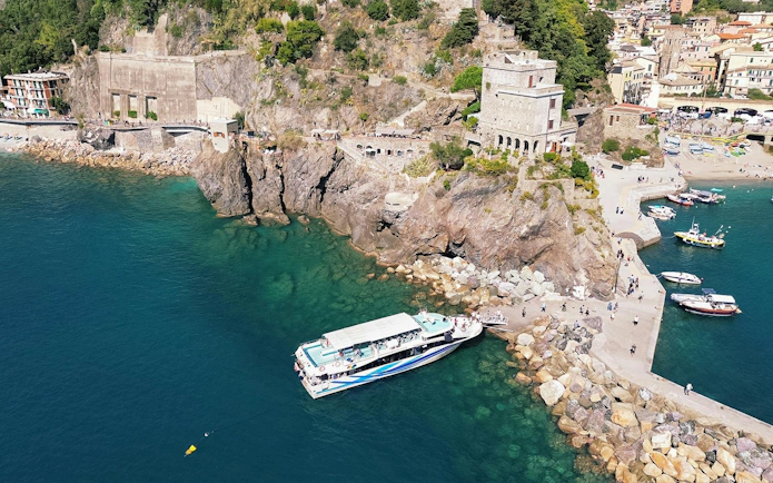 Cinque Terre cruise boat docked near rocky coastline with village in background.