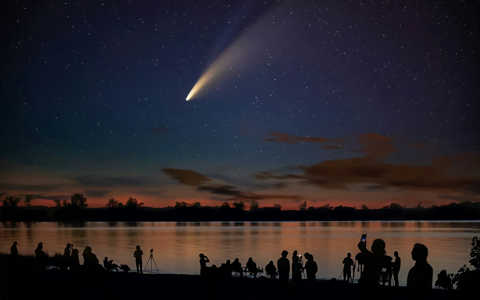 Silhouetted people watching Comet Neowise over a lake at dusk.