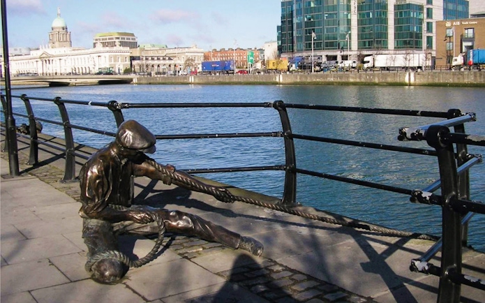 Linesman statue pulling rope on City Quay, Dublin with river and buildings in background.