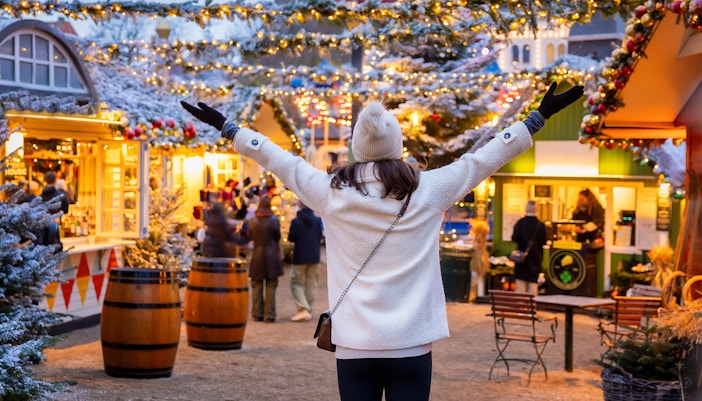 Person enjoying a festive Christmas market with lights and decorated stalls.