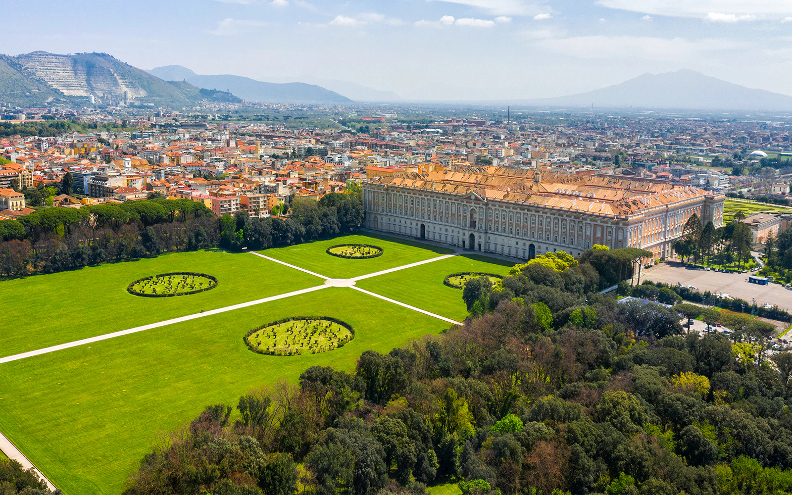 Aerial view of the Garden of Royal Palace of Caserta with expansive lawns and circular hedges.