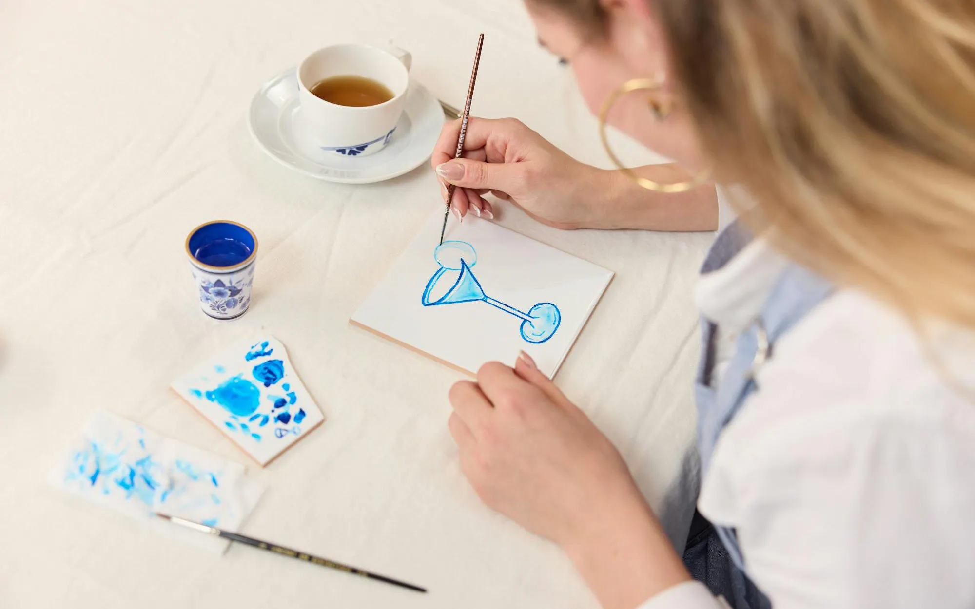 Guest painting blue design on tile at Dutch workshop.