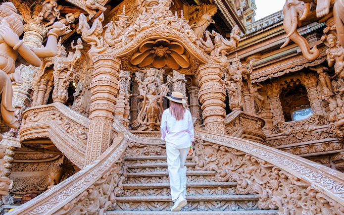 Visitor ascending ornate wooden staircase at The Sanctuary of Truth, Pattaya.