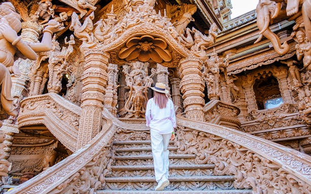 Visitor ascending ornate wooden staircase at The Sanctuary of Truth, Pattaya.
