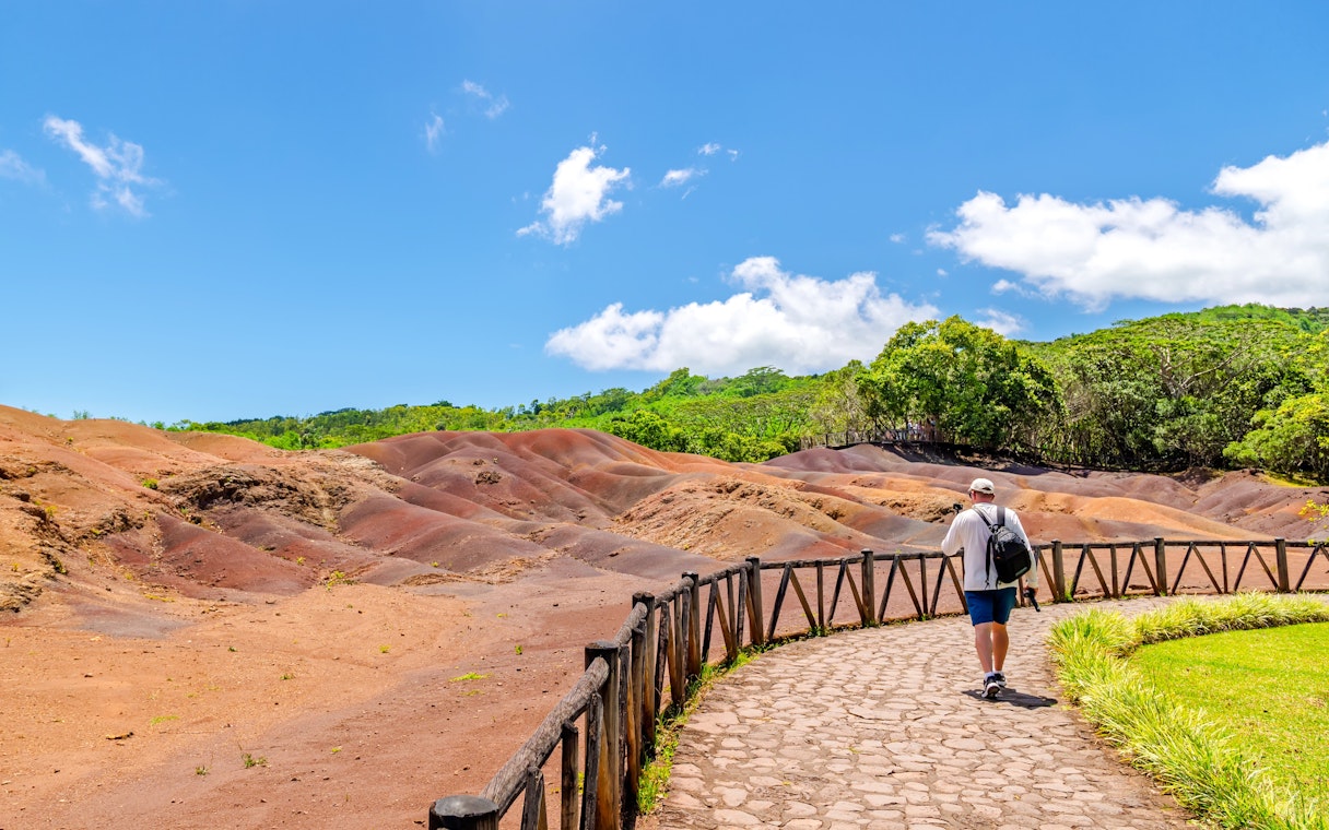 Walker on path beside multicolored volcanic earth dunes in Mauritius.