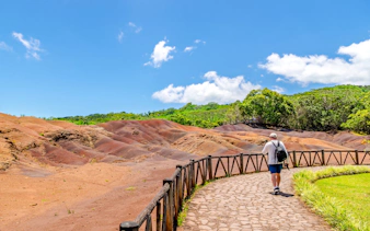 Walker on path beside multicolored volcanic earth dunes in Mauritius.