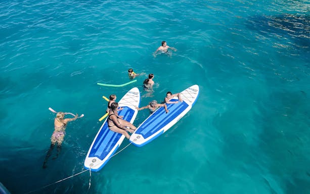 People enjoying paddleboarding and swimming in clear blue waters on a Dreamy Cruise, Kefalonia.
