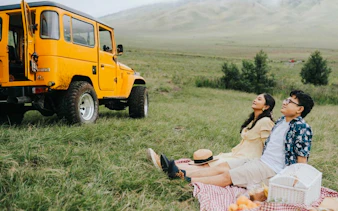 Couple enjoying a picnic near a yellow jeep in Yogyakarta countryside.