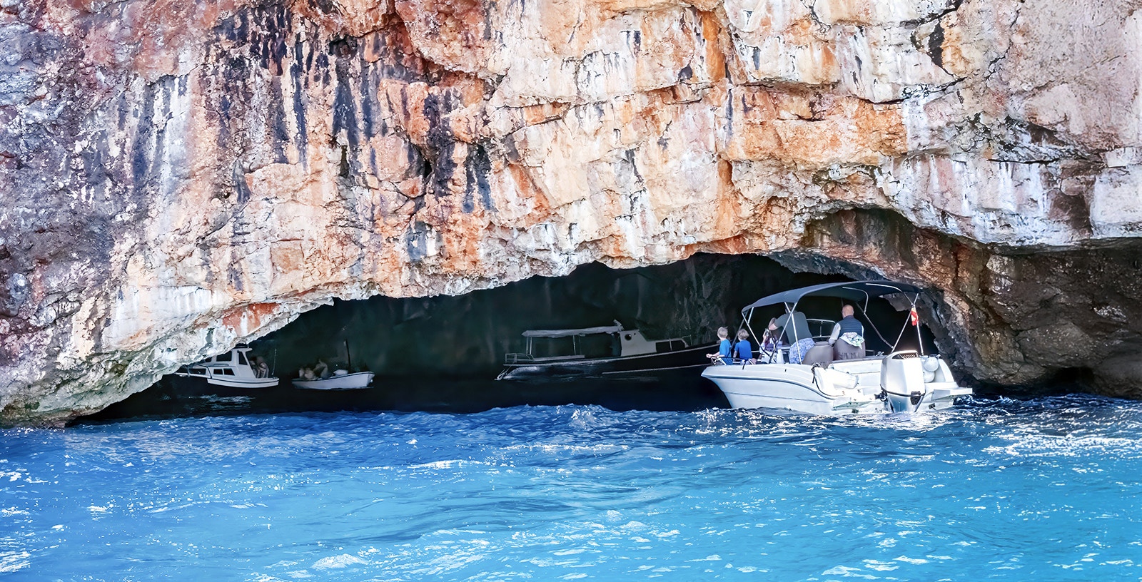 Blue Cave tour boat entering azure waters, Lustica Peninsula, Montenegro.