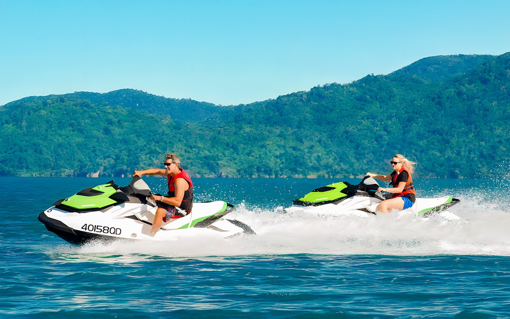 Tourists riding jetskis in the Whitsundays with lush green hills in the background.