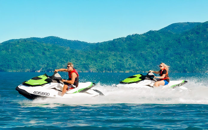 Tourists riding jetskis in the Whitsundays with lush green hills in the background.