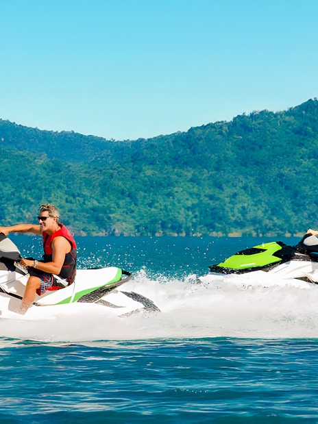 Tourists riding jetskis in the Whitsundays with lush green hills in the background.