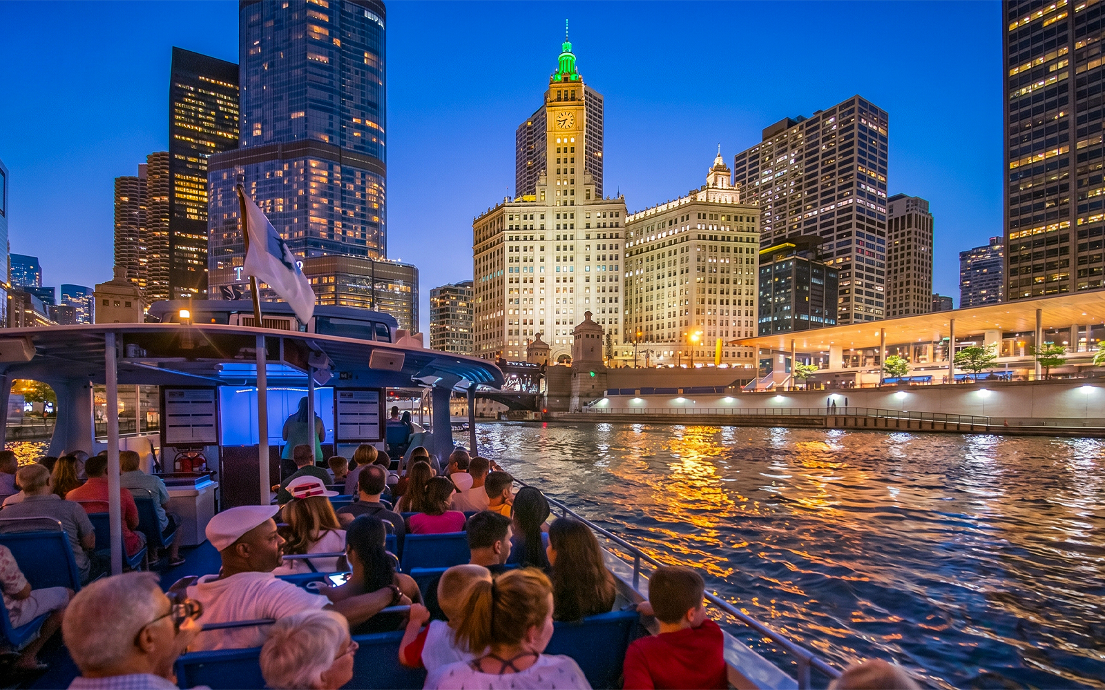 Sightseeing cruise on Chicago River at night with city skyline and Wrigley Building.