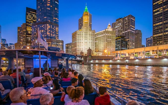 Sightseeing cruise on Chicago River at night with city skyline and Wrigley Building.