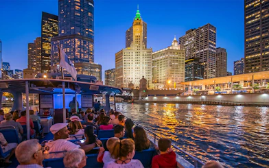 Sightseeing cruise on Chicago River at night with city skyline and Wrigley Building.