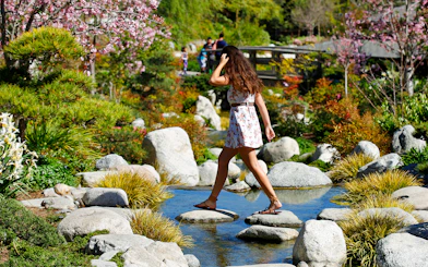 Woman crossing stepping stones in a Japanese garden, San Diego.