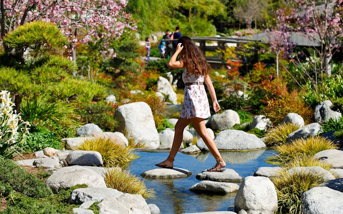 Woman crossing stepping stones in a Japanese garden, San Diego.