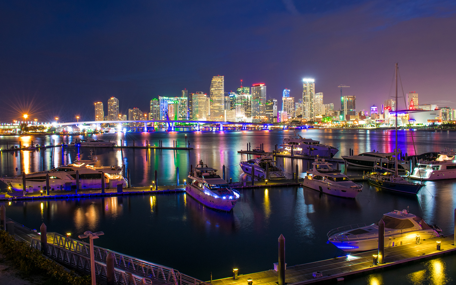 Miami skyline at night with illuminated buildings and yachts in the foreground.