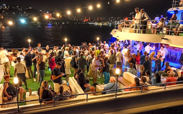 Bosphorus dinner cruise with guests enjoying a Turkish show on a private table under city lights.