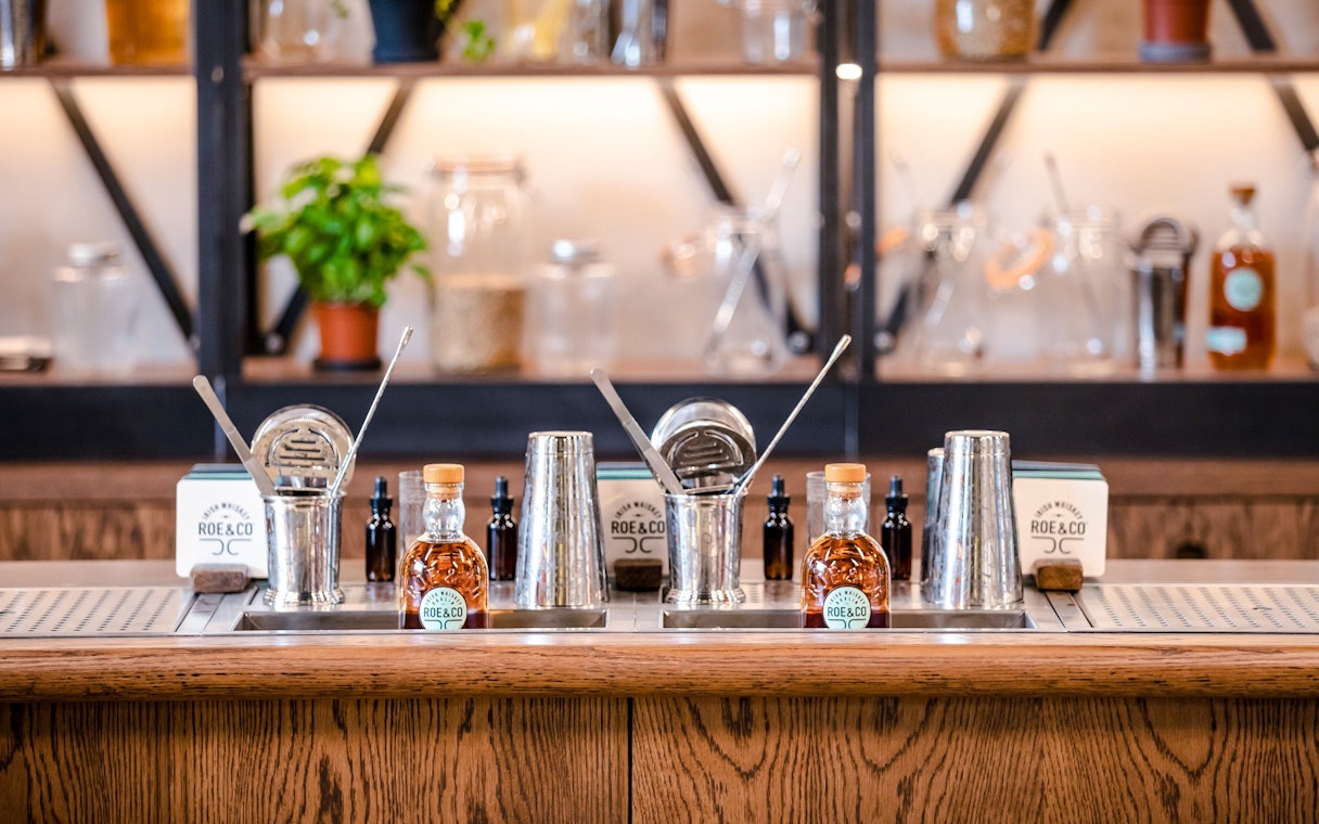 Roe & Co Distillery bar setup with whiskey bottles and cocktail tools.