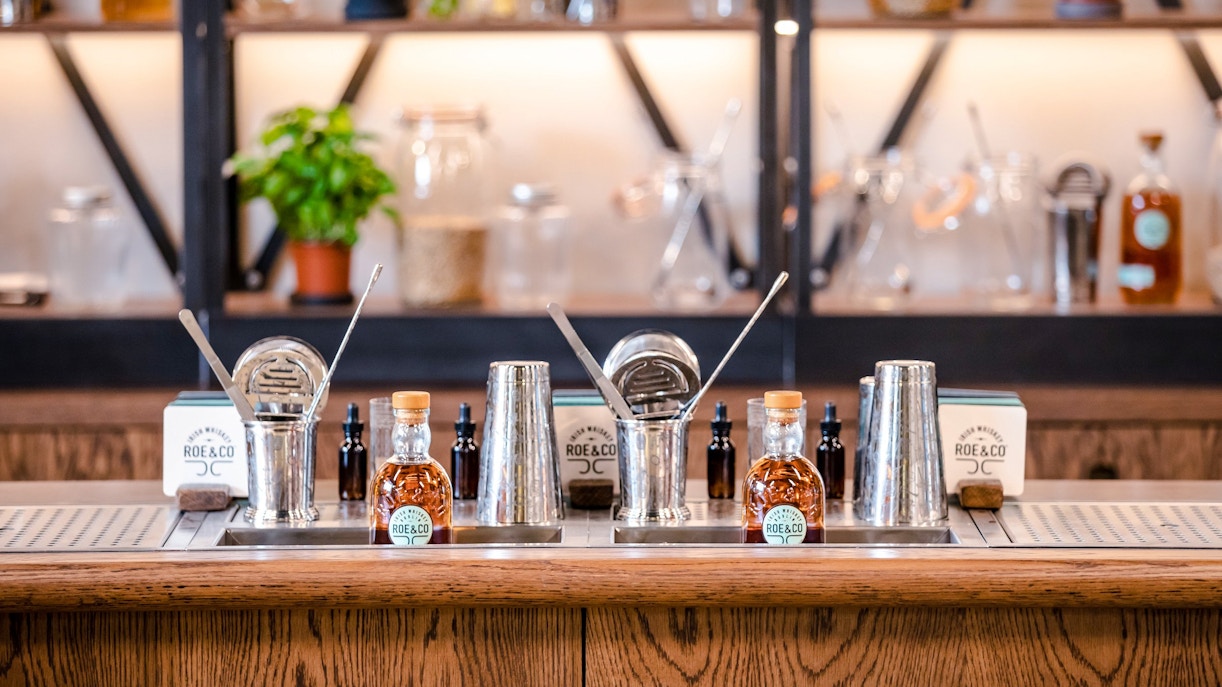 Roe & Co Distillery bar setup with whiskey bottles and cocktail tools.