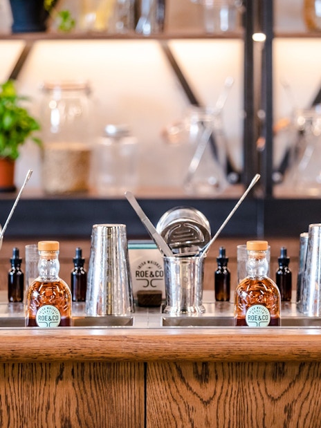Roe & Co Distillery bar setup with whiskey bottles and cocktail tools.