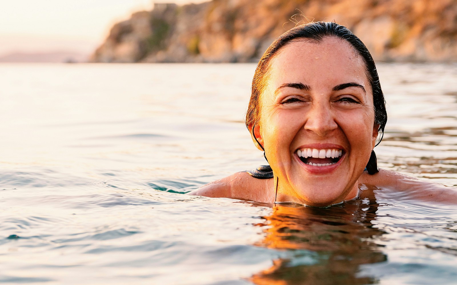 Caucasian woman laughing and showing her white teeth while swimming in sea at sunrise
