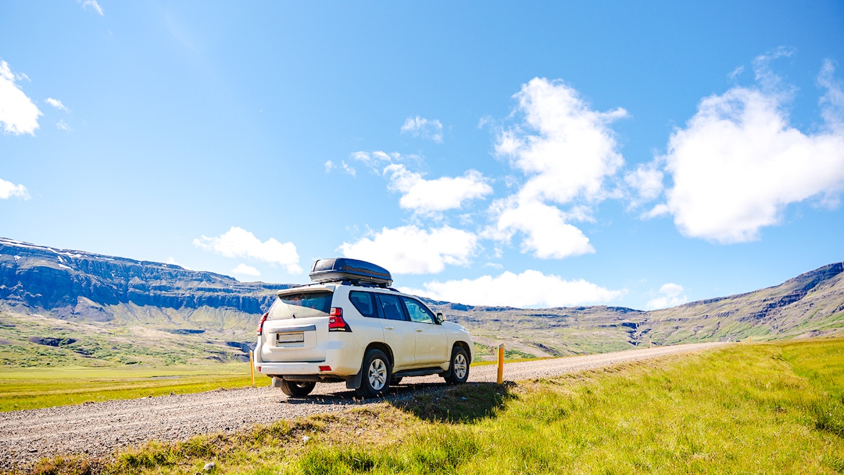 Car on a gravel road in Iceland with mountains in the background.