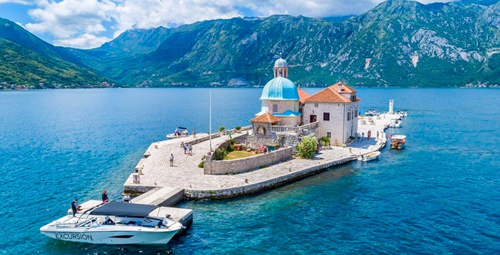 Our Lady of the Rocks Island in Kotor Bay, Montenegro, with surrounding blue waters and mountainous backdrop.