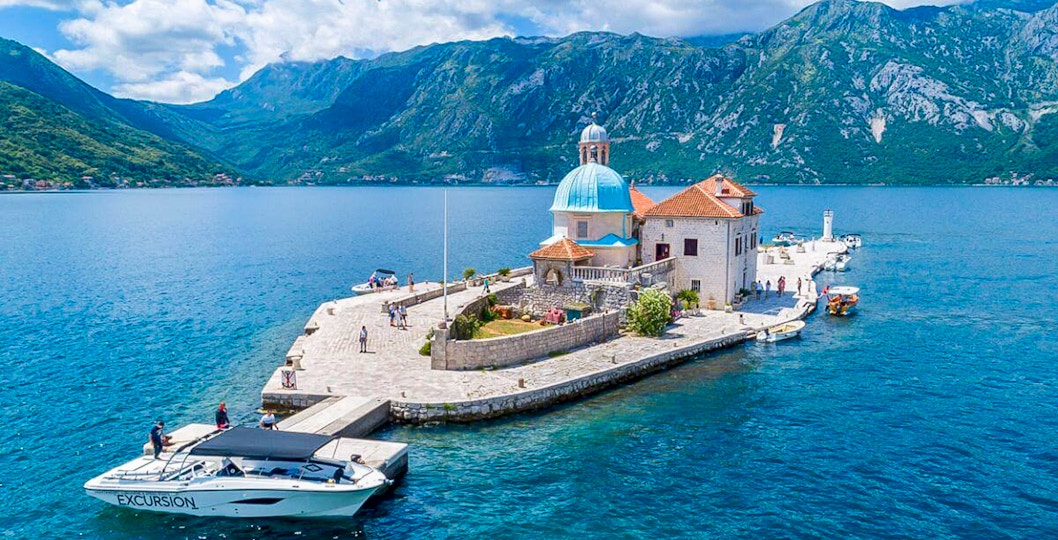 Our Lady of the Rocks Island in Kotor Bay, Montenegro, with surrounding blue waters and mountainous backdrop.