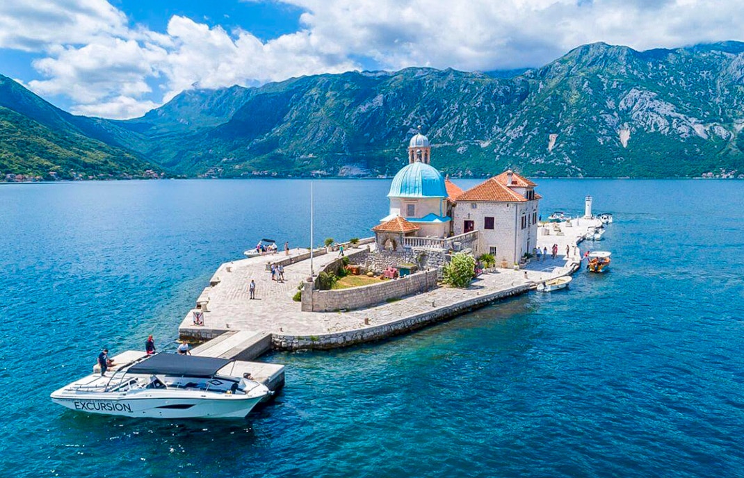 Our Lady of the Rocks Island in Kotor Bay, Montenegro, with surrounding blue waters and mountainous backdrop.