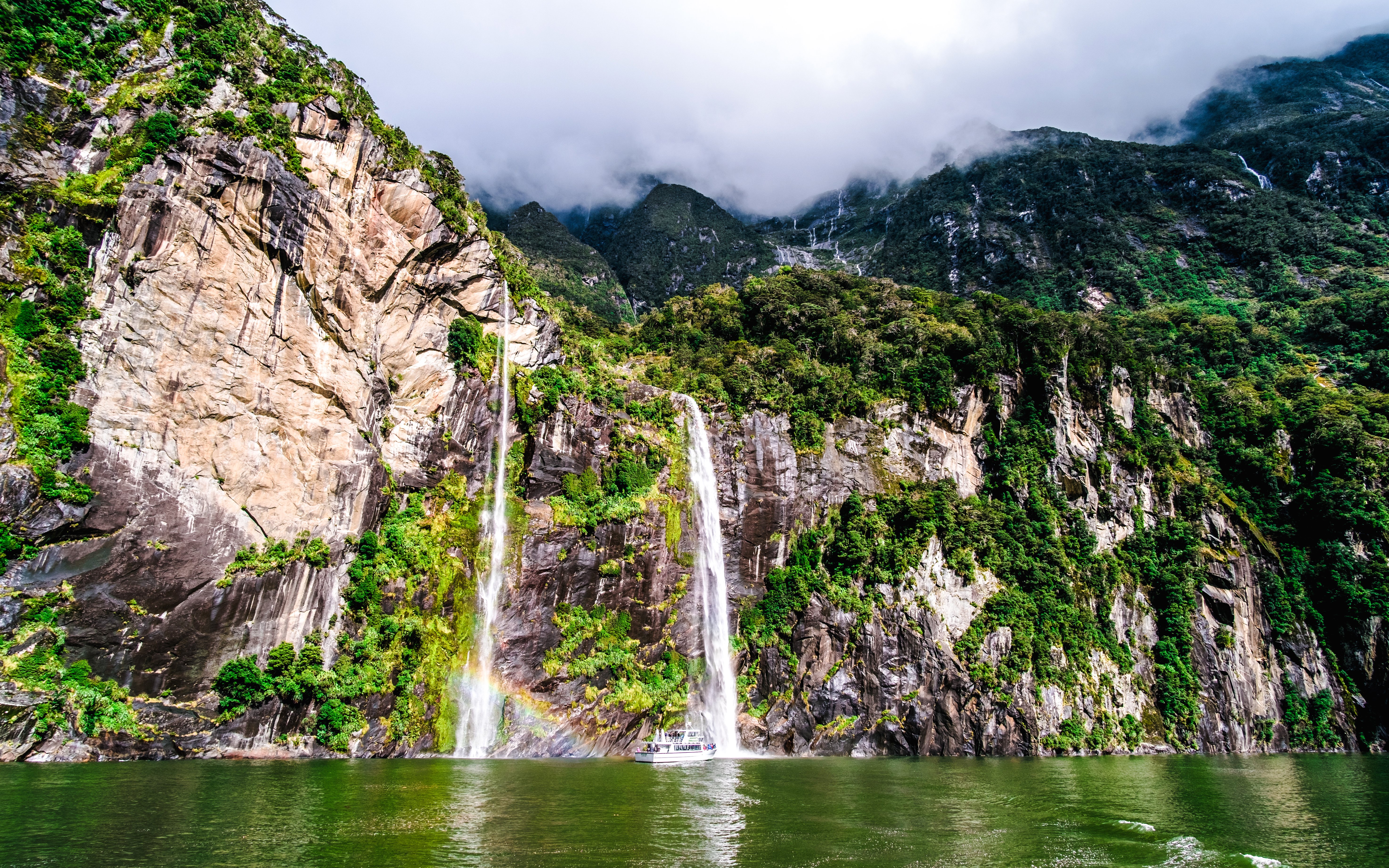 Waterfalls cascading down lush cliffs at Milford Sound, New Zealand.