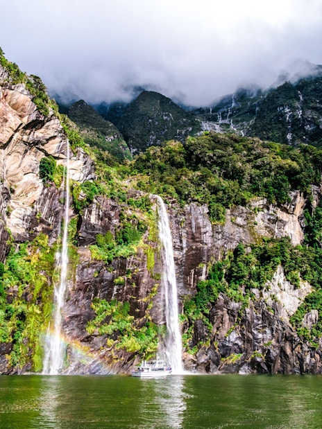 Waterfalls cascading down lush cliffs at Milford Sound, New Zealand.
