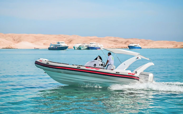 Private speedboat cruising near Orange Bay, Giftun Island, with distant yachts, Hurghada.