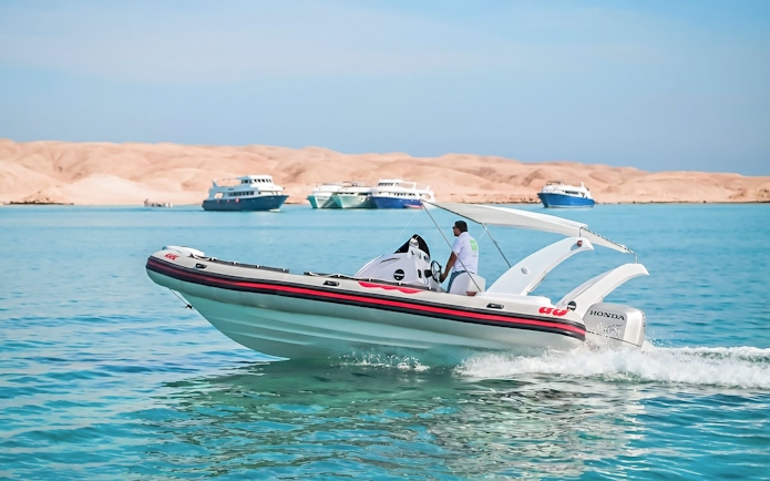 Private speedboat cruising near Orange Bay, Giftun Island, with distant yachts, Hurghada.