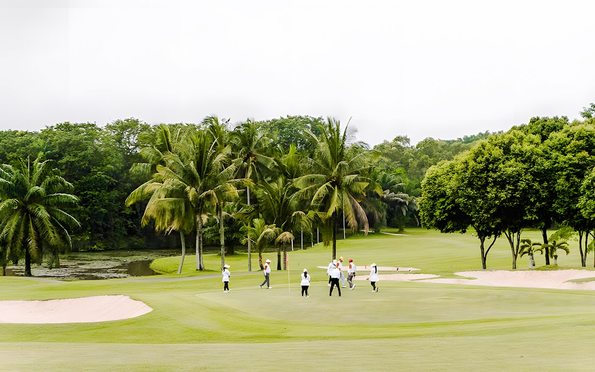 Golfers on the green at Batam Island Country Club, surrounded by palm trees.